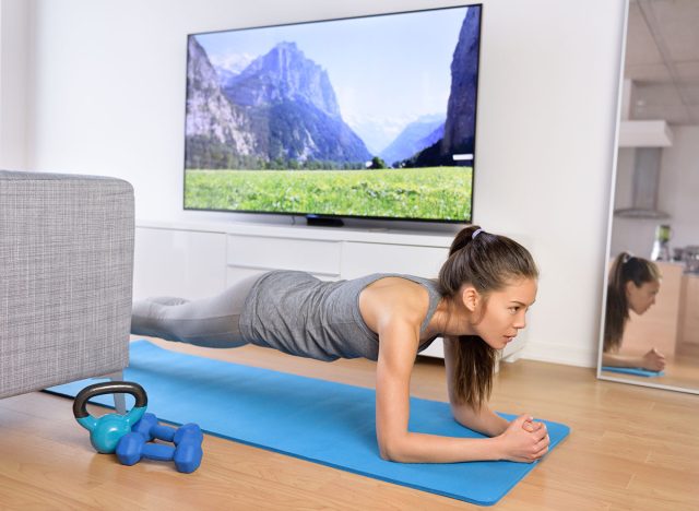 Living room fitness workout - girl doing plank exercises to exercise core at home. Young Asian woman training muscles in front of the TV as part of a healthy lifestyle without going to the gym.