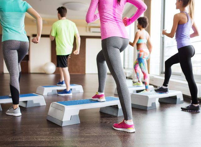 fitness, sport, training, aerobics and people concept - close up of people working out with steppers in gym from back