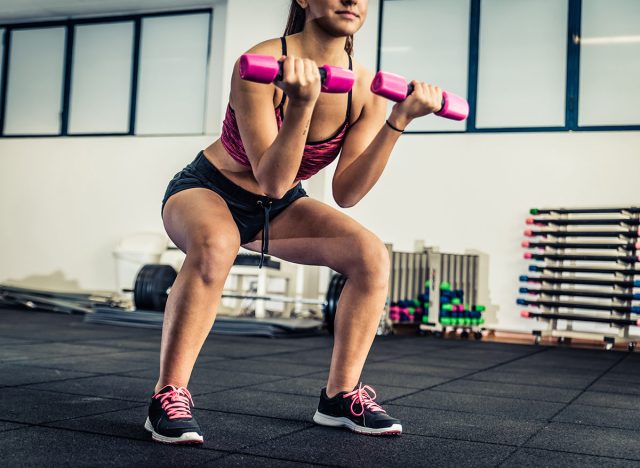Athletic young woman doing squat exercises for the buttocks - Fitness model working out in a gym - Pretty young woman training to stay fit and healthy
