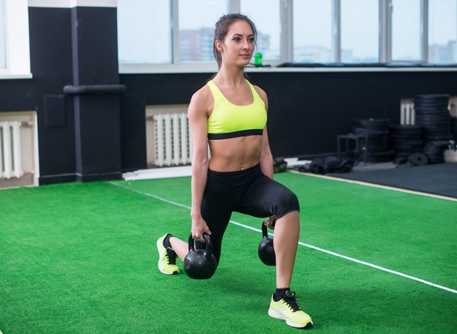 portrait of a sporty woman doing lunges with dumbbells, working out legs muscles