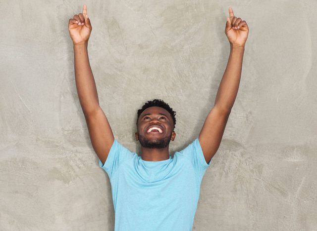 Portrait of carefree young man standing with arms outstretched pointing up