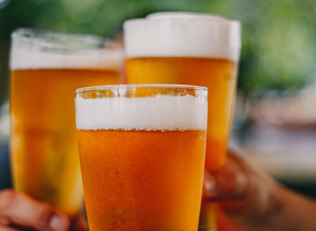 Close-up view of a three glass of beer in hand. Beer glasses clinking at outdoor bar or pub