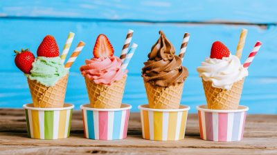 A delicious row of ice cream cones topped with fresh strawberries and colorful straws sitting on a wooden surface.