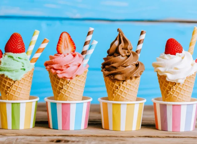 A delicious row of ice cream cones topped with fresh strawberries and colorful straws sitting on a wooden surface.