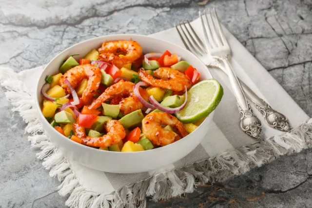Bright rich salad mango shrimp avocado with red onion, bell pepper close-up in a bowl on the table. Horizontal