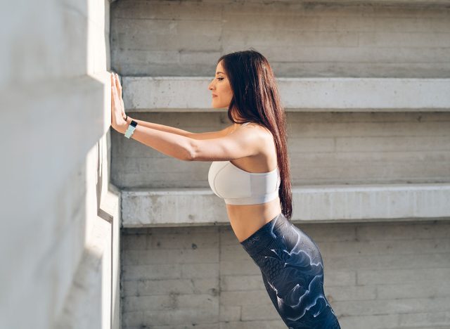 Sporty young woman doing standing wall push up triceps strength exercise during urban outdoor fitness workout.