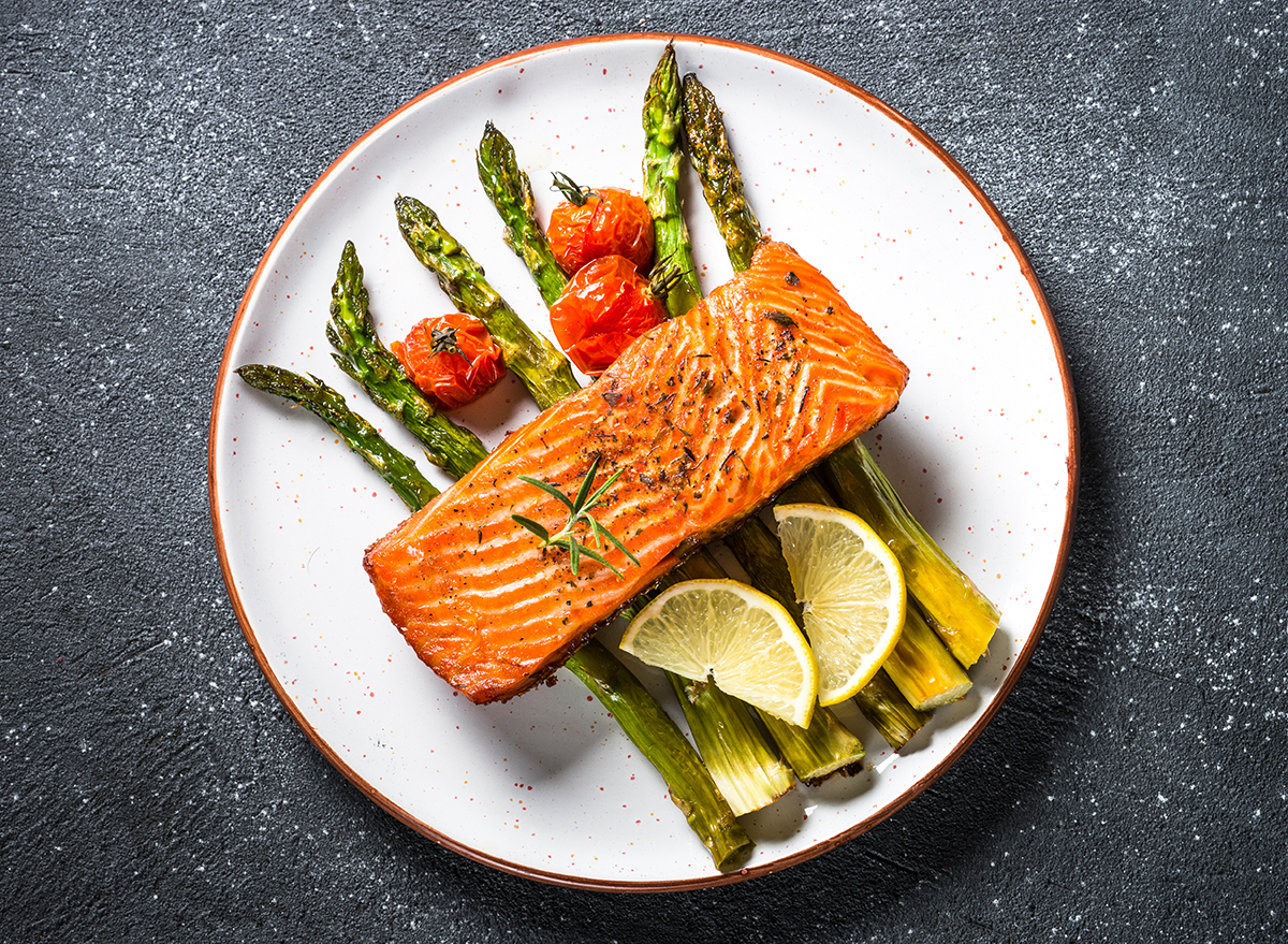 Baked salmon fish fillet with fresh salad from spinach and tomatoes on black stone table. Top view.