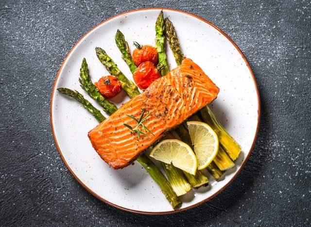 Baked salmon fish fillet with fresh salad from spinach and tomatoes on black stone table. Top view.