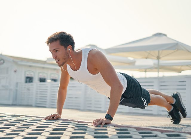 Picture of a young athletic man doing push ups, leg over leg listening music outdoors. Strength and motivation.