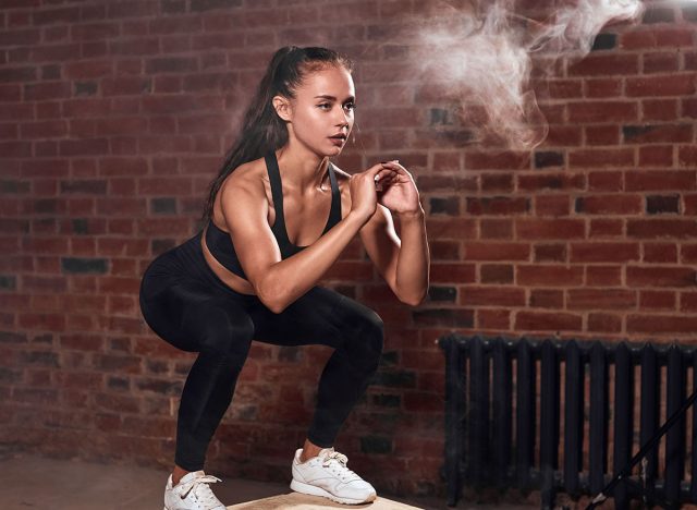 Slim sport woman in sportswear jumping on fit box and do squats. bodybuilding. Brickwall background