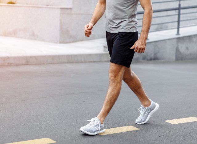 Fitness man athlete runner walking on the road. Person running working out living an active lifestyle training cardio in summer in sportswear and shoes. Lower body banner crop. Close up.