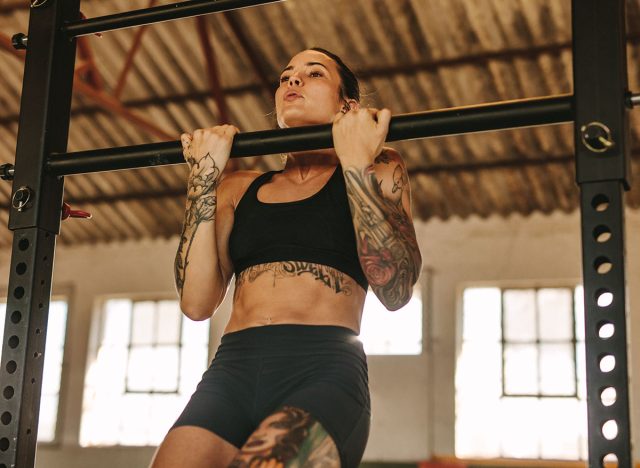 Female doing pull up workout in empty factory shade. Tattooed woman in sportswear exercising at an abandoned warehouse.