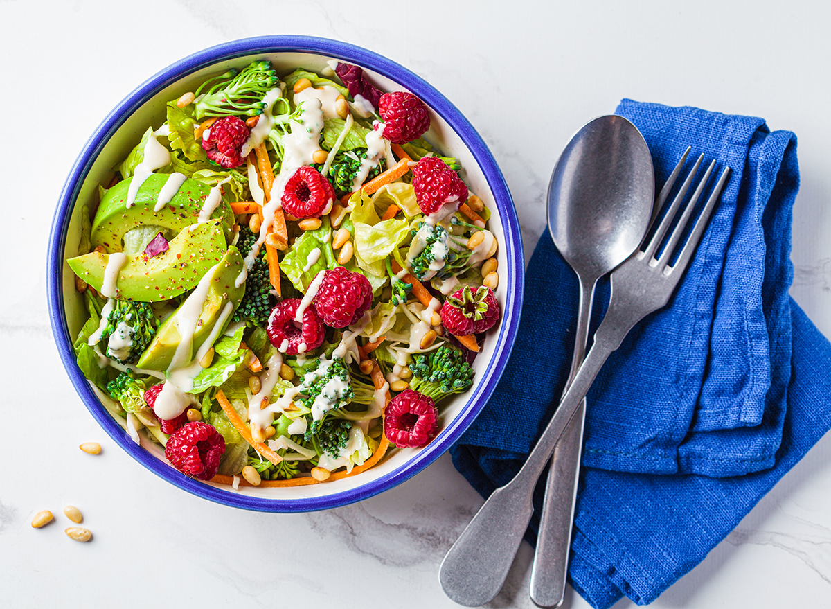Green broccoli salad with raspberries, pine nuts, avocado and tahini dressing, top view. Vegan food concept.