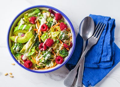Green broccoli salad with raspberries, pine nuts, avocado and tahini dressing, top view. Vegan food concept.