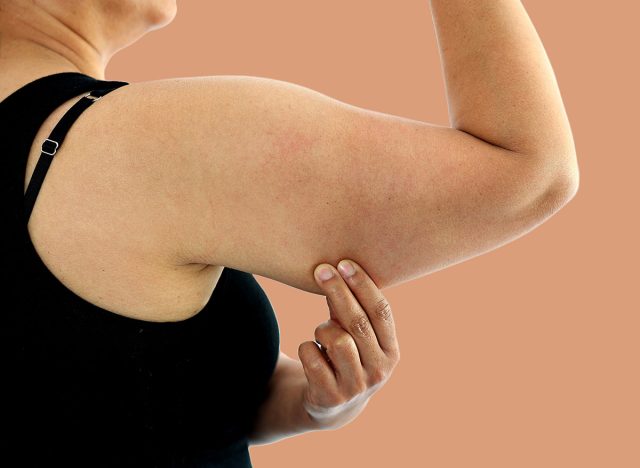 A young Asian woman grabbing skin on her upper arm with excess fat isolated on a white background. Pinching the loose and saggy muscles. Overweight concept