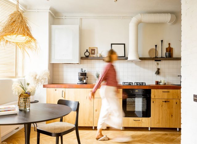 Stylish kitchen interior of modern apartment with motion blurred female person walking inside. Interior made in white and beige tones with wooden kitchen front and floor