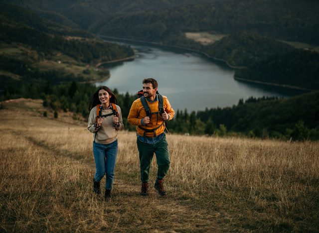 A couple explores nature, enjoying the beauty of an evening hike. The lake visible in the background