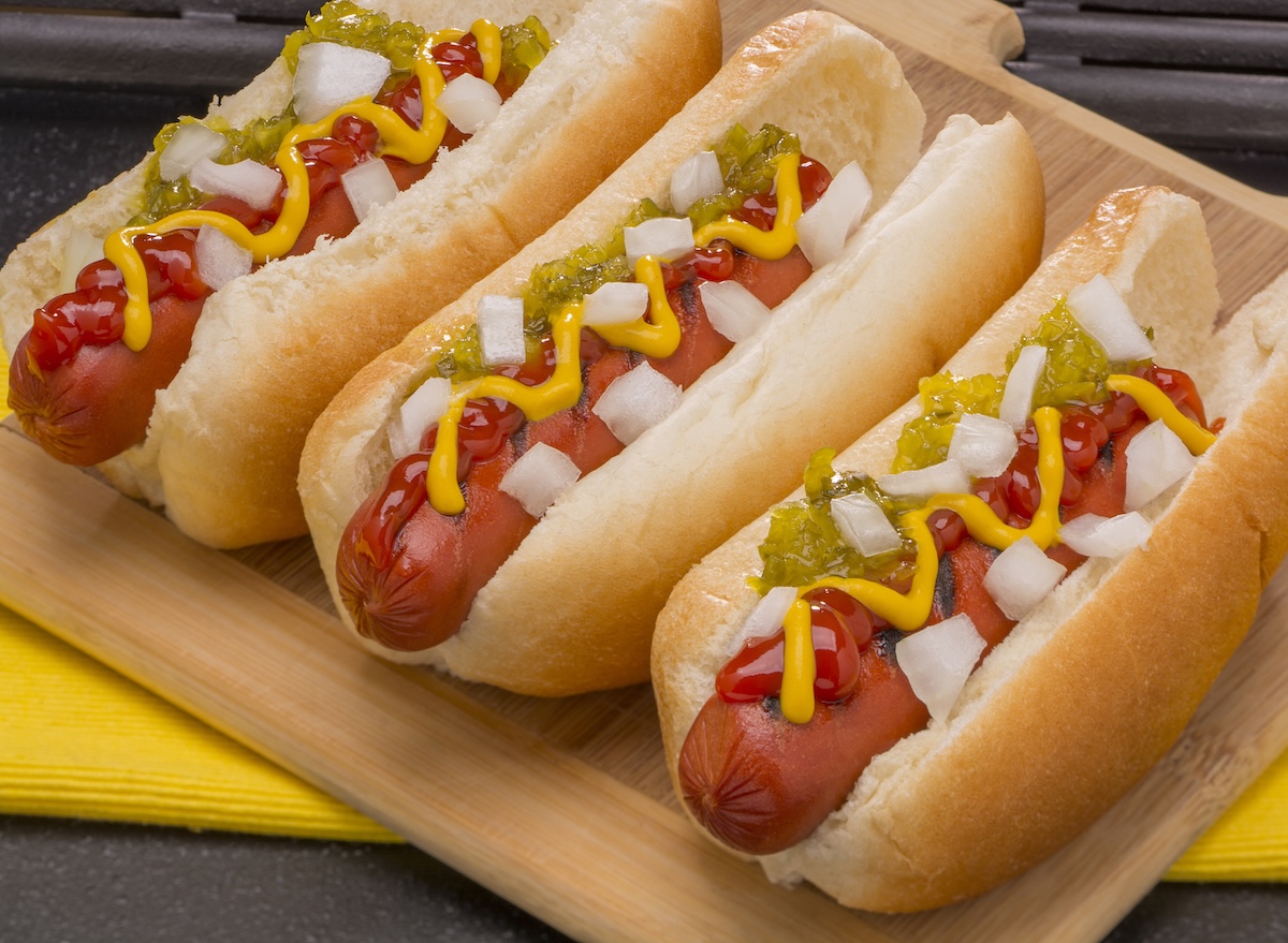 Three,Hot,Dogs,With,Mustard,,Ketchup,,Pickle,Relish,And,Onions