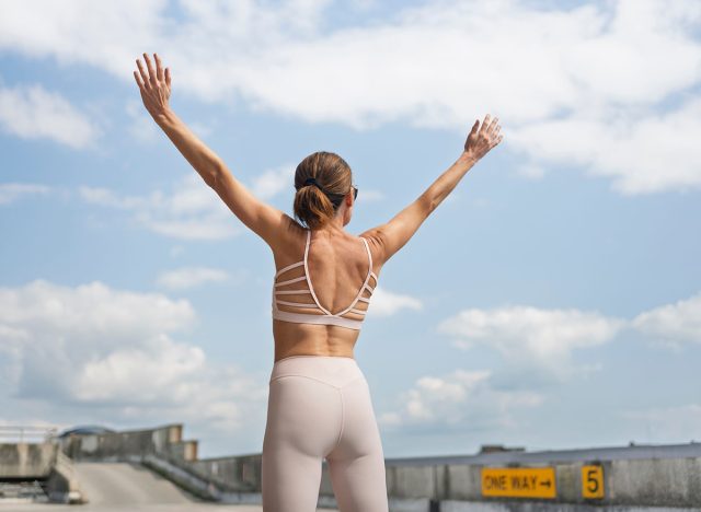 fit sporty woman with arms raised outdoors, freedom concept