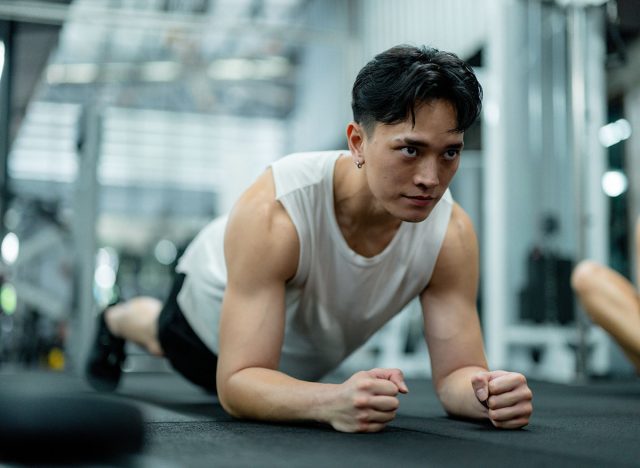 Young man doing plank exercise on fitness mat, training core muscles in modern gym