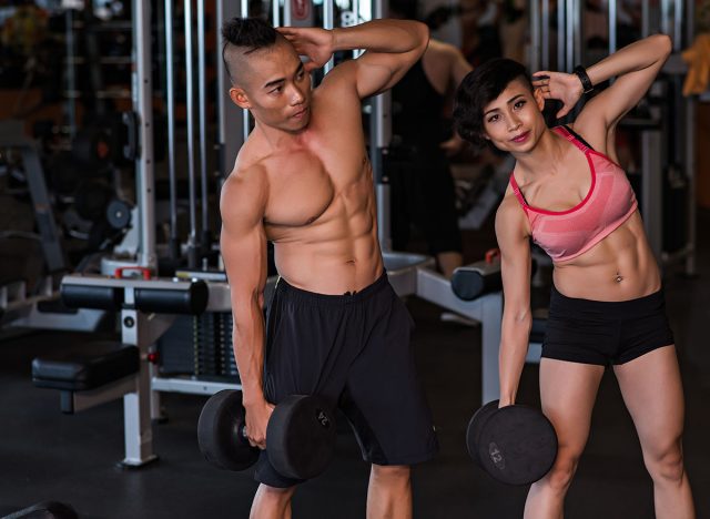 Vietnamese young couple doing dumbbell side bends together in the gym