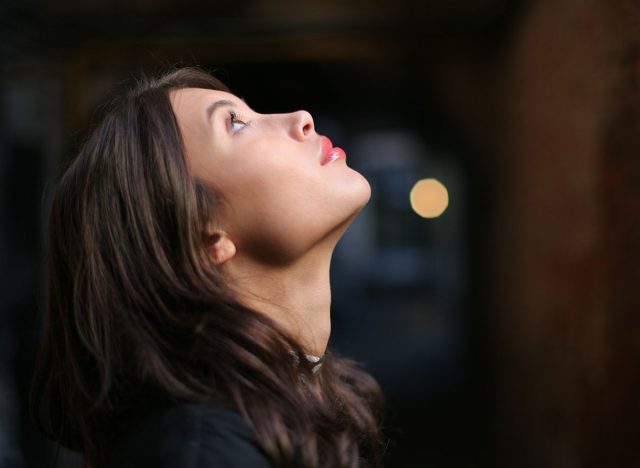Profile portrait of beautiful young woman looking up over dark background. Closeup on face, shallow DOF.