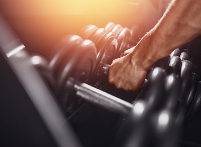 Close-up man grabs a heavy dumbbell in gym with his hand. Concept lifting, fitness.