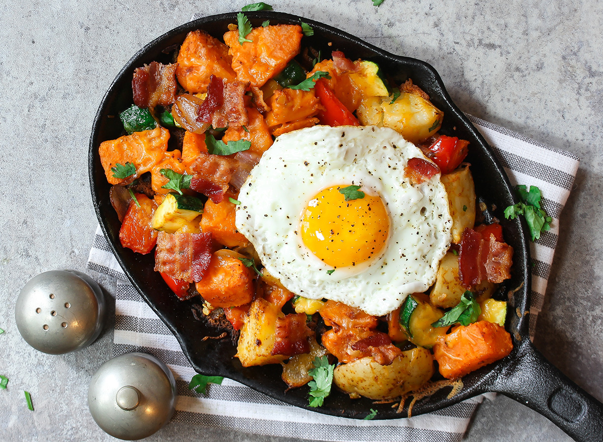 Skillet Breakfast Hash with potatoes bacon peppers sweet potatoes cheese Zucchini and fried egg, top view with copy space