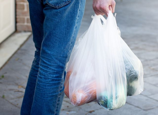 Man walking and holding plastic shopping bags with various fruits and groceries. Environment pollution, waste problem, rubbish, trash.