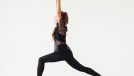Young sporty attractive woman practicing yoga, doing Warrior I exercise, Virabhadrasana 1 pose, working out, wearing sportswear, black pants and top, indoor full length, white yoga studio