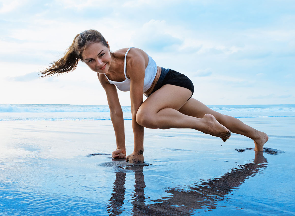 Sporty woman doing mountain climber exercise - run in plank to burn fat. Sunset beach, blue sky background. Healthy lifestyle at tropical island yoga retreat, outdoor activity, family summer vacation.