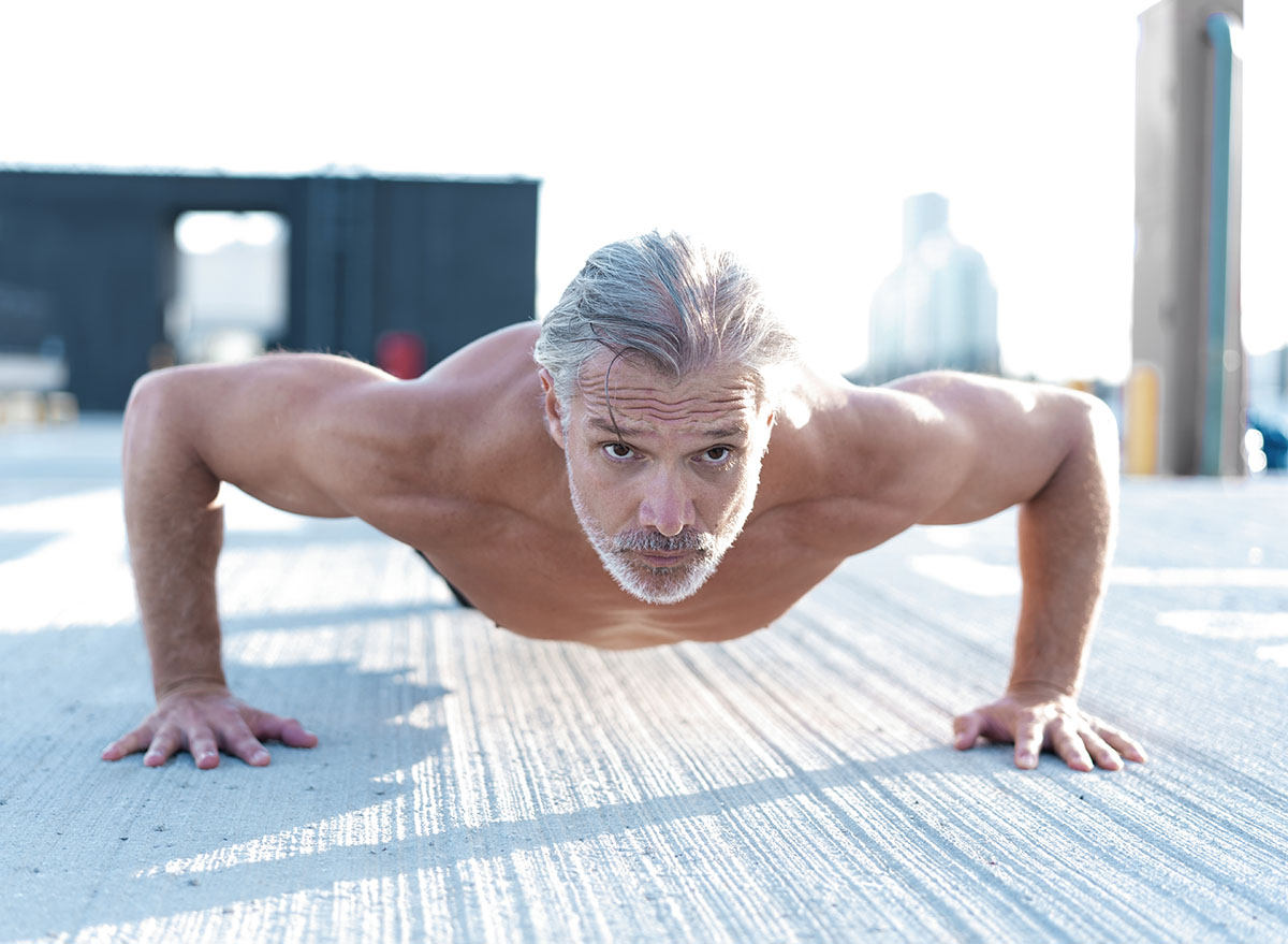 Middle-aged athletic man doing push ups outdoors. Fitness and exercising outdoors urban environment.