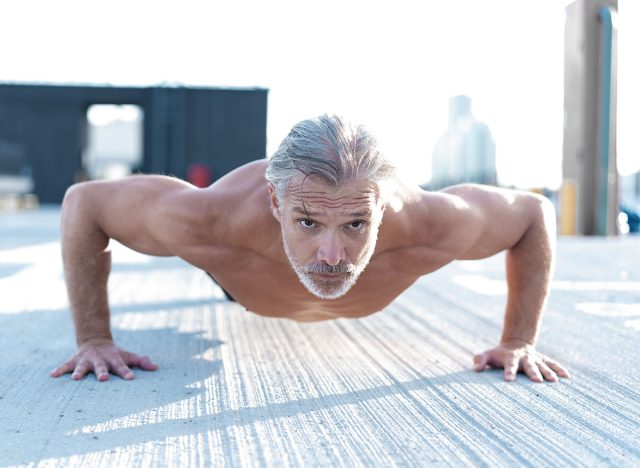 Middle-aged athletic man doing push ups outdoors. Fitness and exercising outdoors urban environment.