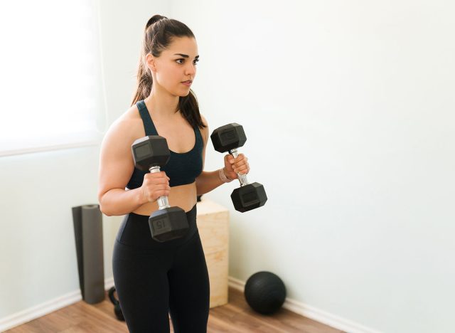 Attractive young woman exercising with two dumbbells. Sporty woman with muscular arms lifting weights to work out her athletic body