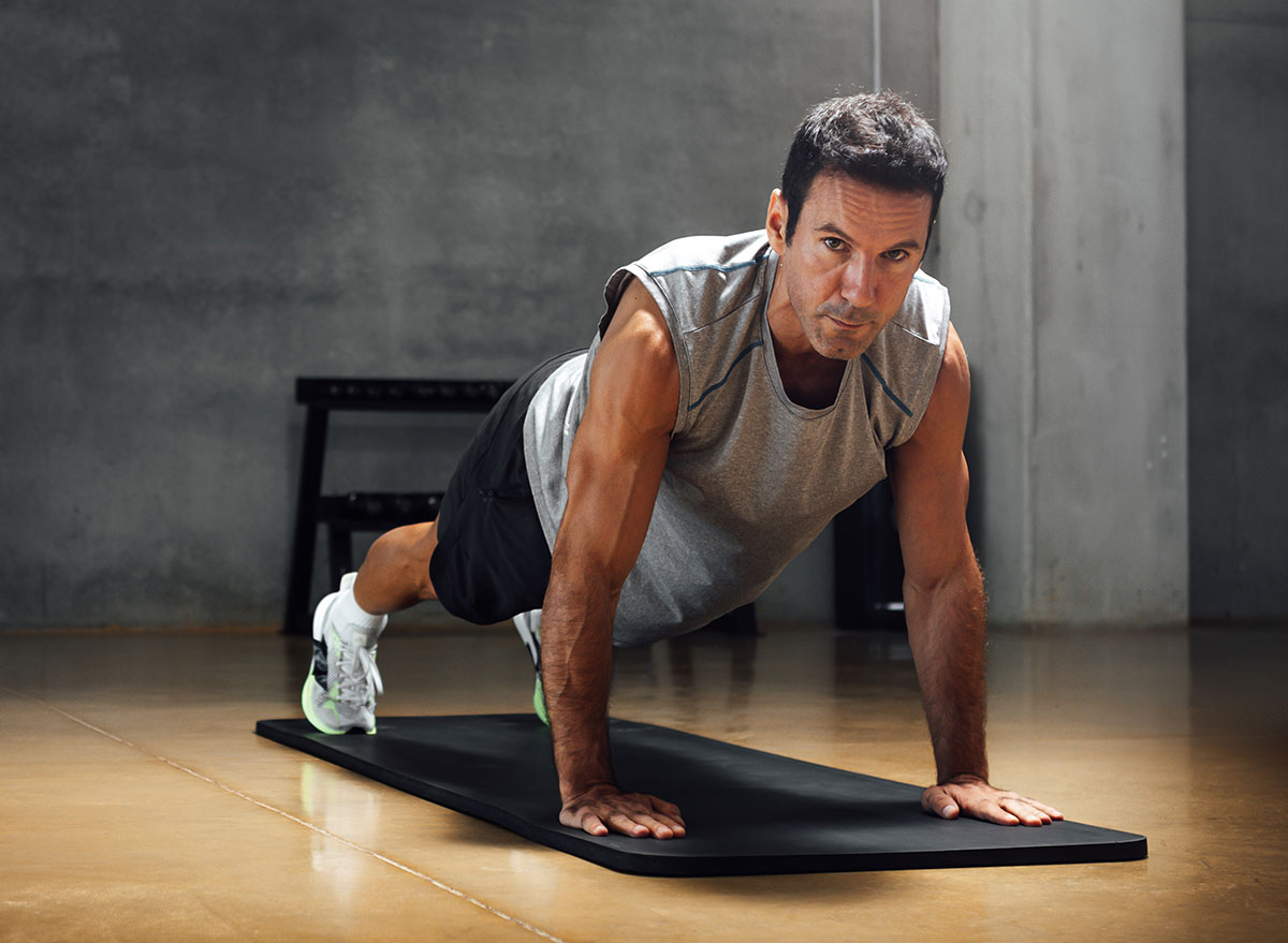 Strong caucasian man does push-ups while looks at camera in a dark gym.