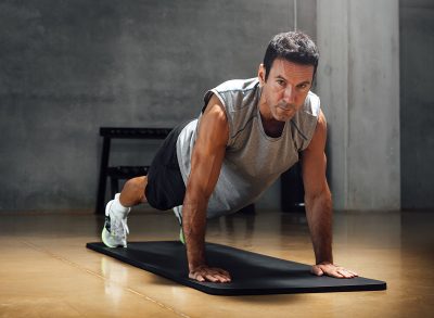 Strong caucasian man does push-ups while looks at camera in a dark gym.