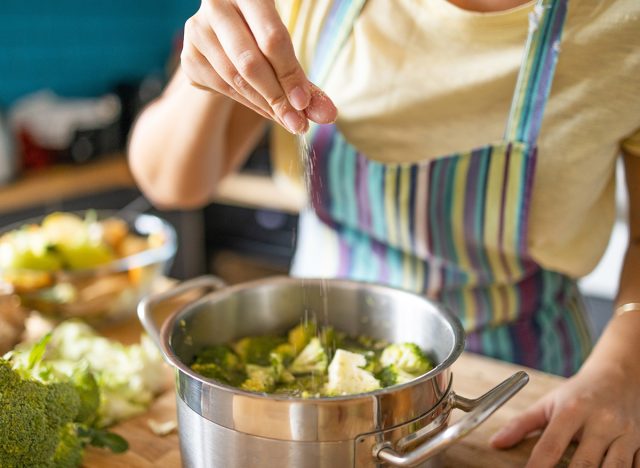 Young woman adding spices to lunch, seasoning food 