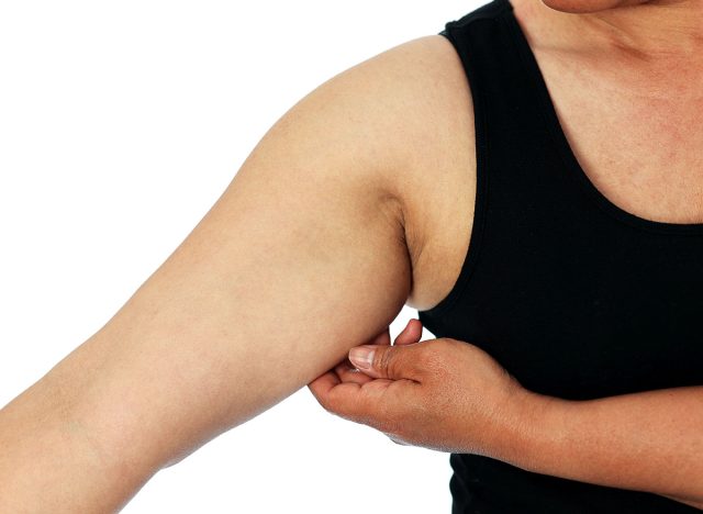 A young Asian woman grabbing skin on her upper arm with excess fat isolated on a white background. Pinching the loose and saggy muscles. Overweight concept
