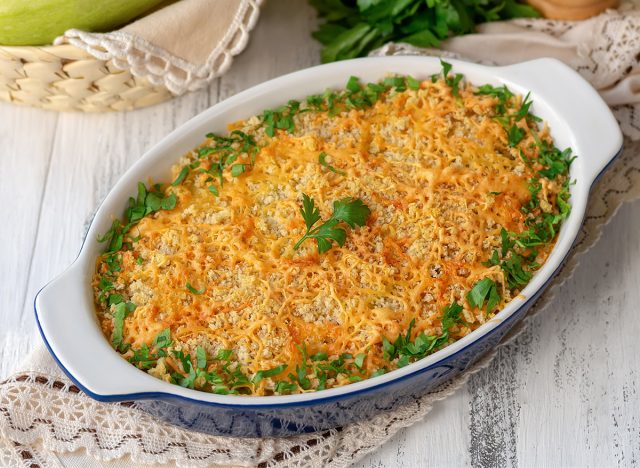 Baked summer squash gratin with bread crumbs, grated cheese, olive oil and parsley in oval ceramic baking dish. Light wooden background, selective focus