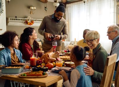 Happy multigeneration family having Thanksgiving dinner in dining room. Focus is on African American man serving wine to his wife.