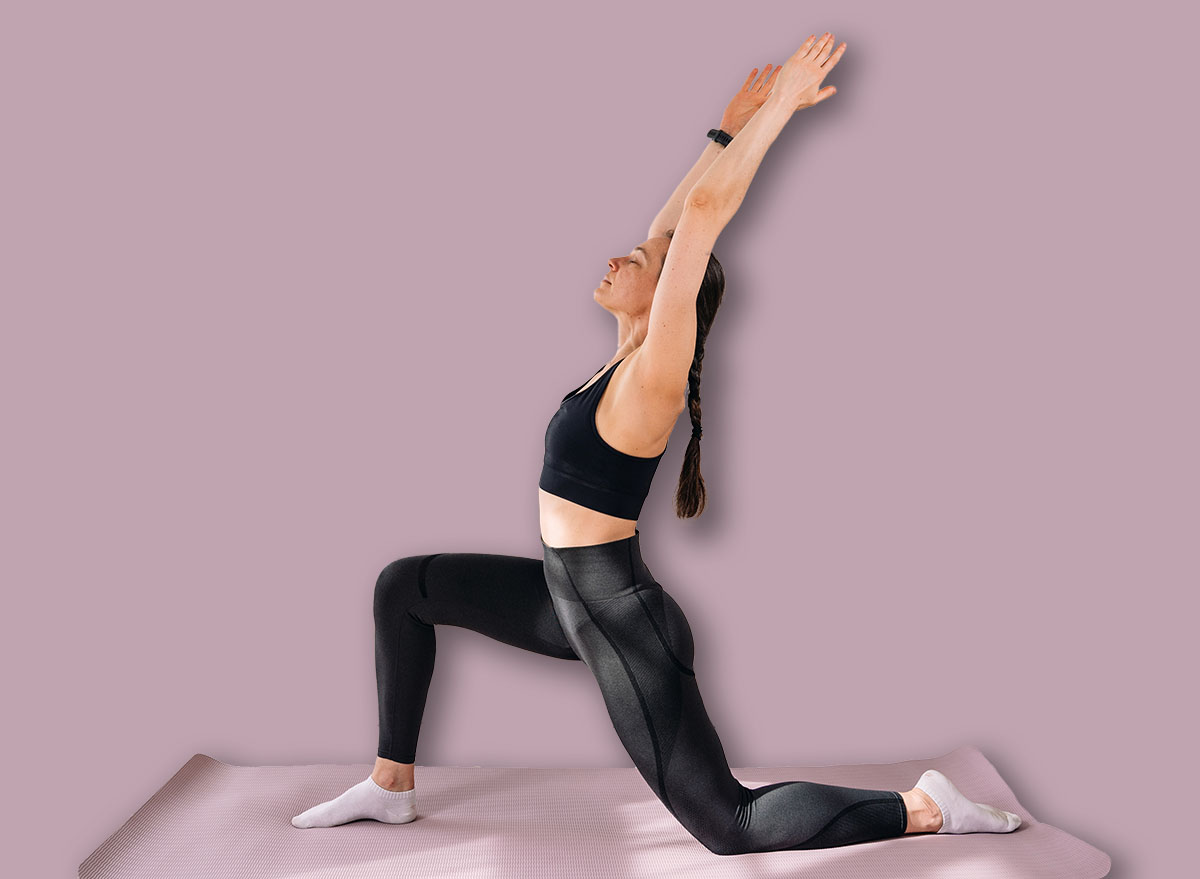 A young woman practices a fitness exercise on a yoga mat in her living room. She stretches in a bright apartment, promoting a healthy lifestyle and physical activity. Yoga concepts