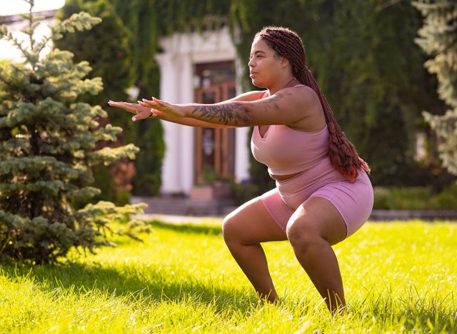 Plus size young woman doing squats on the lawn and looking determined
