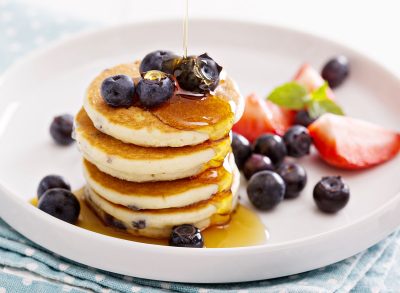 Stack of small pancakes with fresh berries and syrup