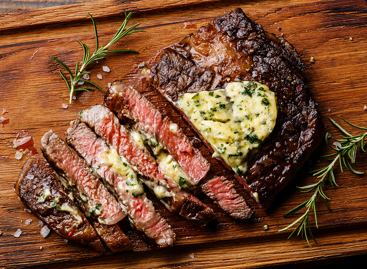 Sliced grilled Medium rare barbecue steak Ribeye with herb butter on cutting board close up