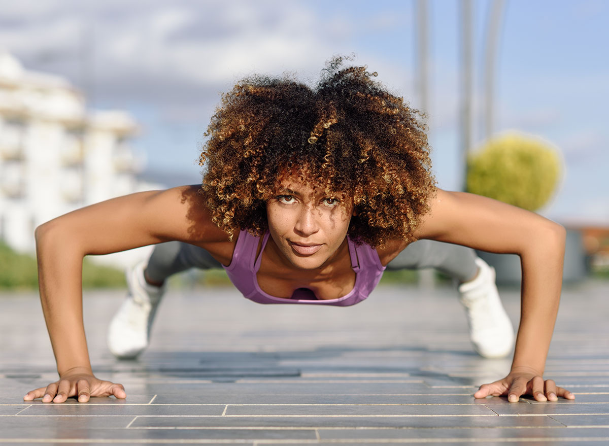 Black fit woman doing pushups on urban floor. Young female working out in the street.