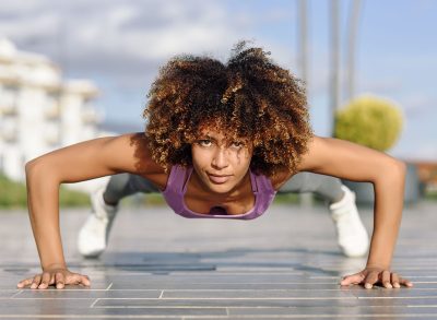 Black fit woman doing pushups on urban floor. Young female working out in the street.