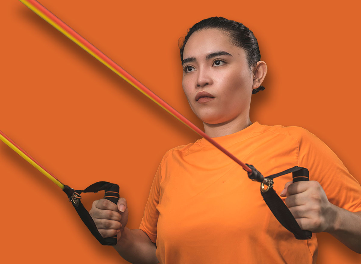 A fit and novice asian woman does standing back rows with a resistance band. Working our and training at a home gym.