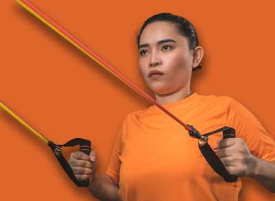 A fit and novice asian woman does standing back rows with a resistance band. Working our and training at a home gym.