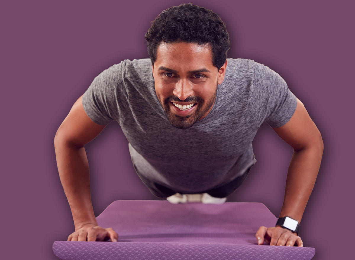 Man In Fitness Clothing At Home In Lounge Doing Press Ups And Exercising With Hand Weights