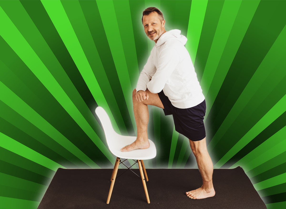 Senior man using a chair to do stretch exercises in a home gym in an effort to keep fit during the Covid-19 pandemic turning to smile at the camera